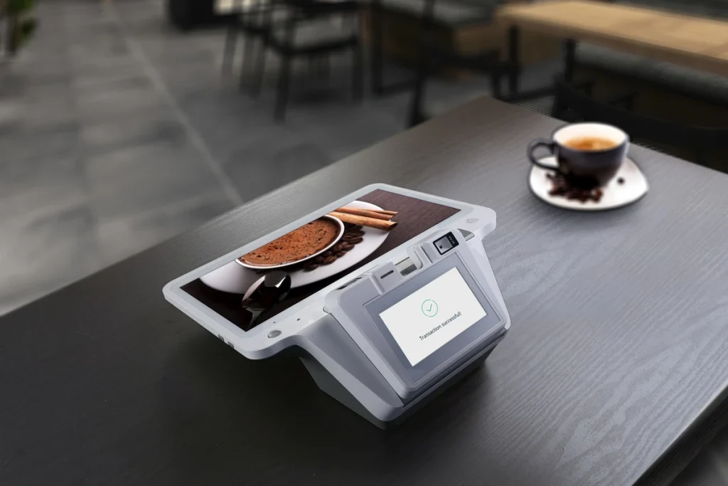 A countertop payment terminal on a cafe table beside an espresso
