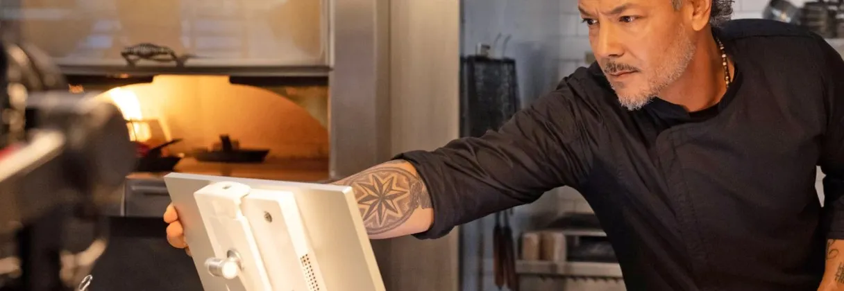 Chef reading order tickets on a Clover kitchen display beside a pizza oven